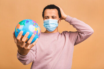 Cheerful african american black man holding the globe with love and care isolated over beige background. Travel concept, looking for a jorney. Coronavirus concept, hygienic protective mask.