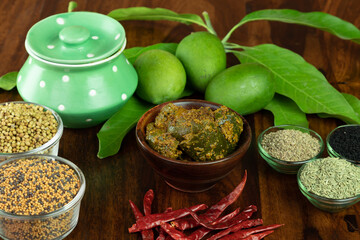 Mango Pickel or Homemade Mango Pickle or aam ka achar or Kairi Loncha in a wodded bowl with Spices and jar and Raw Mango, selective focus