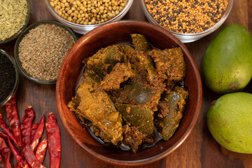 Homemade Mango pickle or Aam ka Achar top view with indian spices and chillies and raw mango isolated on wooden background