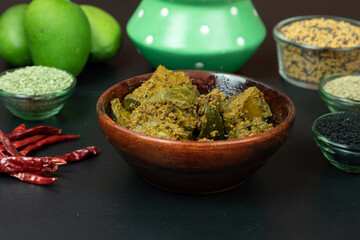 Mango Pickel or Homemade Mango Pickle in a wooden bowl with chillies and indian spices, selective focus, isolated on black