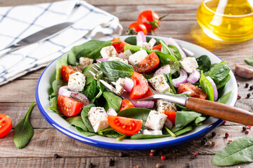Fresh vegetables salad from spinach, tomato, feta cheese, onion in plate on a wooden table