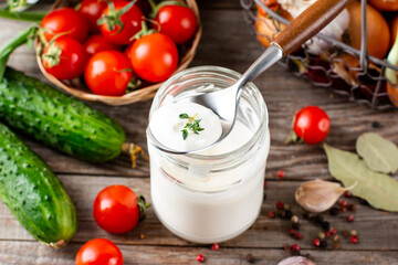 Sour cream in a jar with vegetables on the background. Dressing for vegetables and salads