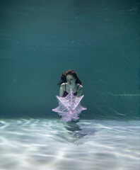 beautiful girl in a red swimsuit with a pink umbrella underwater on a blue background