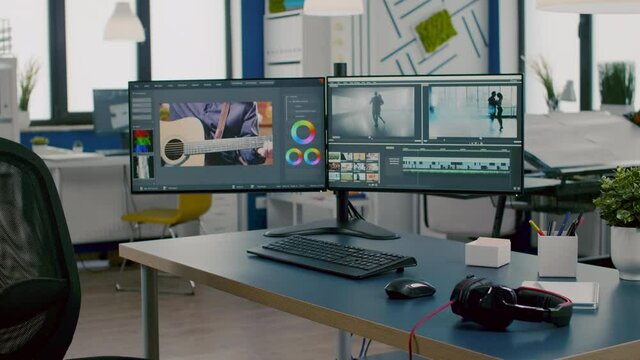 Modern creative workplace with nobody in and dual displays setup processing video film montage. Video editing start up studio company with no people in it and post production software on pc displays