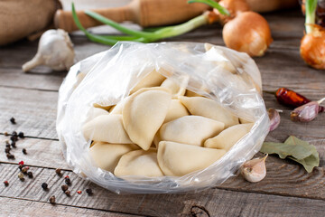 Traditional Russian dumplings, ravioli, meat dumplings on a wooden table. Rolling pin, napkin, garlic, onion, bay leaf and spices.