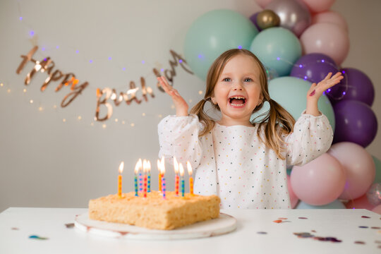 cute little girl blows out candles on a birthday cake at home against a backdrop of balloons. Child's birthday