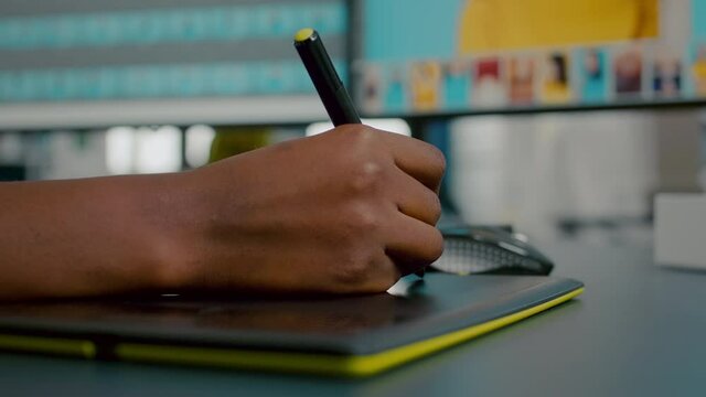 Close up of photo designer editing with tablet and pencil, illustrator drawing on graphics tablet. Hand of african woman retoucher using stylus pen retouching assets sitting in creative agency office
