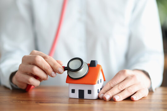 Person listens through stethoscope to wall and roof of house