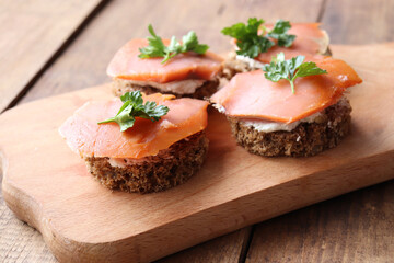 Smoked salmon avocado canapes on rye bread with cream cheese and parsley. Sandwich with salmon on cut board on wooden background. Midsummer party food. Top view
