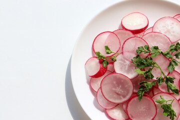 Fresh radish salad with parsley on white background. Top view, copy space. Spring summer vegetable salad on white plate