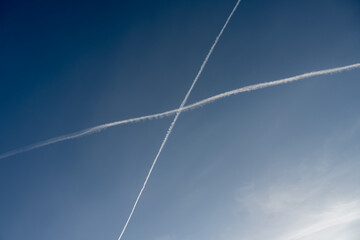Fototapeta na wymiar White trails, from jet exhaust, form a cross in the sky. A blue sky on the background