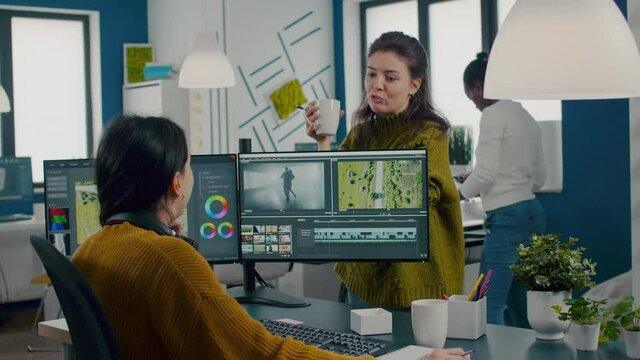 Team of videographers talking about project while working in video editing app at computer with dual monitors setup sitting in modern digital multimedia company. Creatice women prosessing film montage