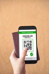Hand holding a passport and a smartphone with a Covid19 immunity certificate