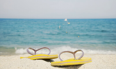 A pair of flip-flops left on the beach. Sand, blurred water waves, sunny day. Summer vacation...