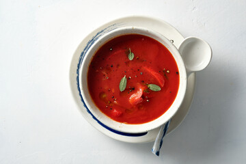 Tomato soup in a white bowl on white background. Top view. Copy space