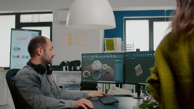 Mechanical engineer working on computer designing in CAD software 3D model of engine while african coworker asking help. Man using pc with two monitors innovating motor prototype in creative agency