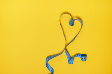 blue measuring tape in the form of heart on yellow background
