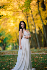 Beautiful brunette young female in white dress in autumn park