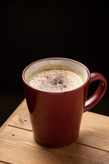 Aerial view of cup of cappuccino coffee on wooden table, dark background, vertical, with copy space