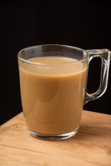 Close-up of glass cup of coffee with milk, on wooden table, dark background, vertical, with copy space