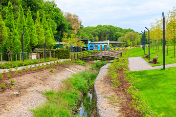 Fototapeta premium Beautiful view of the city park with arched footbridge across small river and young trees