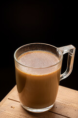 Aerial view of glass cup of coffee with milk, on wooden table, black background, vertical, with copy space