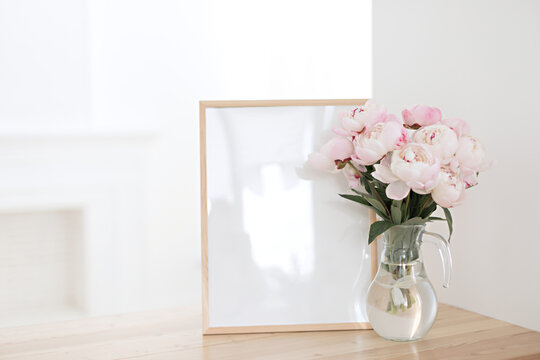 Vertical frame mocap on a wooden table in the kitchen. Glass vase with a bouquet of pink peonies and a cup of black coffee. Scandinavian style interior.
