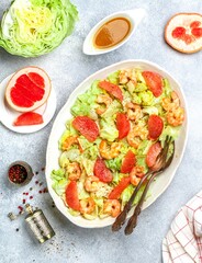 Shrimp (prawn)  salad with grapefruit slices, fresh lettuce and olive oil and mustard dressing with spices and seasonings in a white plate on a gray concrete background. Selective focus