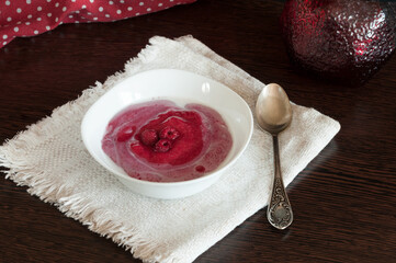 Berry mousse with raspberries and milk in a white plate on a dark table. Selective focus