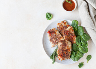 Fried turkey or chicken breast served with orange sauce, spinach and rosemary on a plate, light concrete background. Healthy balanced food. Top view.