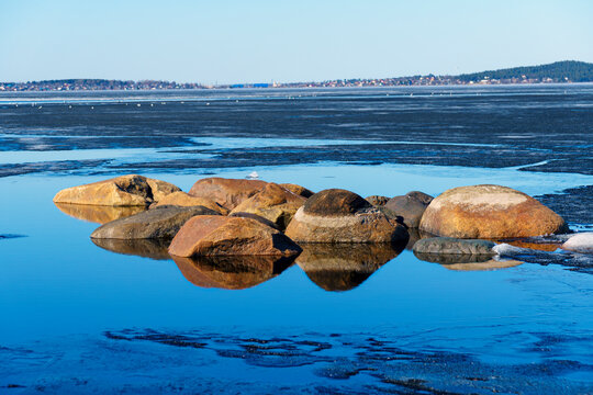 Landscape with stones stick out from calm lake bay water and ice in spring