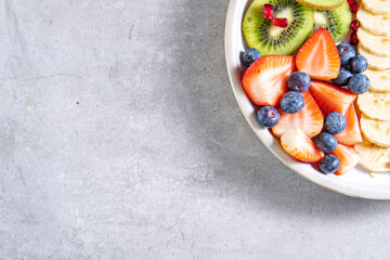 Slice of kiwi, banana, strawberries and blueberries, fruit salad on plate.