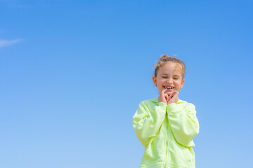 Portrait of beautiful little girl in yellow sweet on a blue sky background. Happiness concept, active childhood, carefree, summer lifestyle.