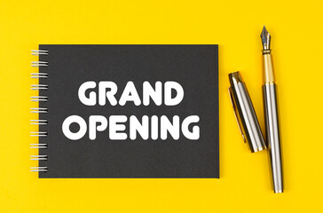On a yellow background lies a pen and a black notebook with the inscription - Grand Opening