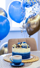 Handmade birthday cake on a blurred background with balloons and sparkles. Cheesecake cake, blue and gold accents. Festive background for postcard, holiday, birthday, anniversary, 18 years. 