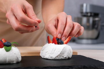 Obraz na płótnie Canvas Hands of pastry chef decorates cake with fresh strawberries and blueberries. Cake Anna Pavlova