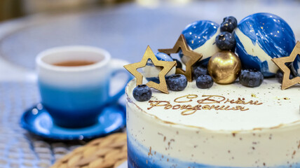 Handmade birthday cake on a blurred background with balloons and sparkles. Cheesecake cake, blue and gold accents. Festive background for postcard, holiday, birthday, anniversary, 18 years. 