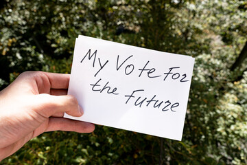 Male hand holds white paper with "My vote for the future" inscription. Vote and Make a choice image concept.