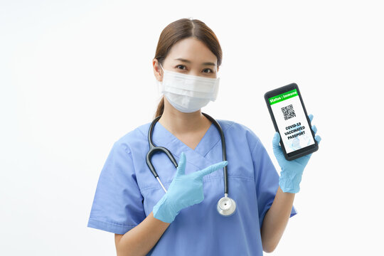 Young Asian woman in the nurse uniform with stethoscope and wearing protective facemask  point her finger the smartphone to show Covid-19 vaccinated passport application, concept vaccination campaign.