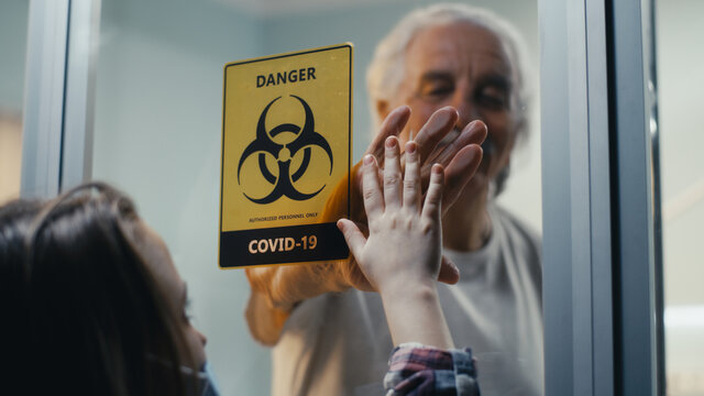 Senior Man Touching Hand Of Granddaughter Behind Glass Wall In COVID Ward