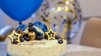 Handmade birthday cake on a blurred background with balloons and sparkles. Cheesecake cake, blue and gold accents. Festive background for postcard, holiday, birthday, anniversary, 18 years. 