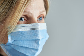 Woman blonde wearing medical face mask on a gray background. Photo with copy space.