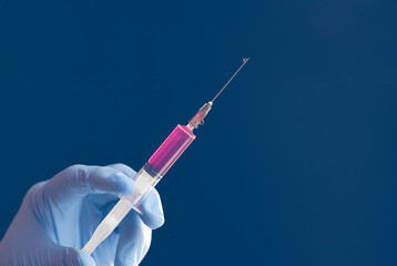 Doctor's blue-gloved hand holding a syringe with red liquid isolated on blue background.
