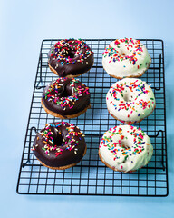 Three chocolate doughnuts and three white chocolate doughnut with colours topping on blue background.