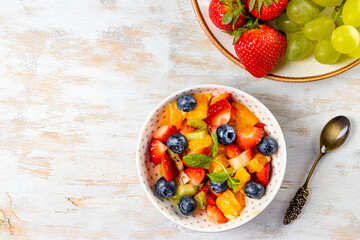 Fresh summer salad of various fruits and berries. Kiwi, orange, strawberry and blueberry on a plate decorated with mint on a wooden white background top view