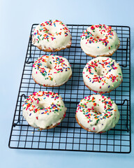 White chocolate donuts on cooling rack with colourful sugar topping on blue background.