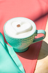 Coffee drink with milk foam heart on pink and mint satin fabric.