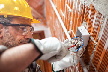 Electrician worker with a screwdriver fixes the cable in the switch of an electrical system; wear...