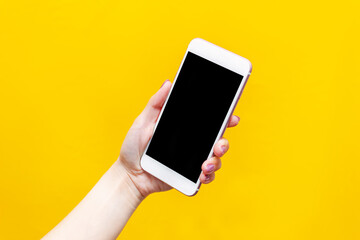 White phone with black screen in female hand isolated on a bright color yellow background. Black blank with an empty copy space for the text. Template for the design. Mockup of a smartphone