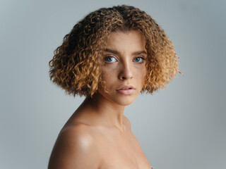 Portrait of a beautiful woman on a light background curly hair naked shoulders blue eyes